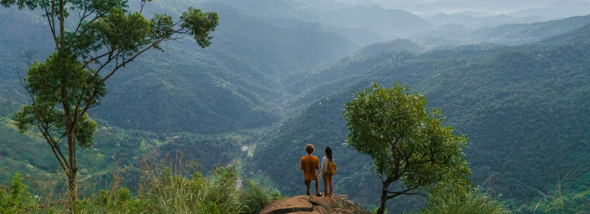 Aerial view of man and woman standing on Ella rock and looking at lush green hills